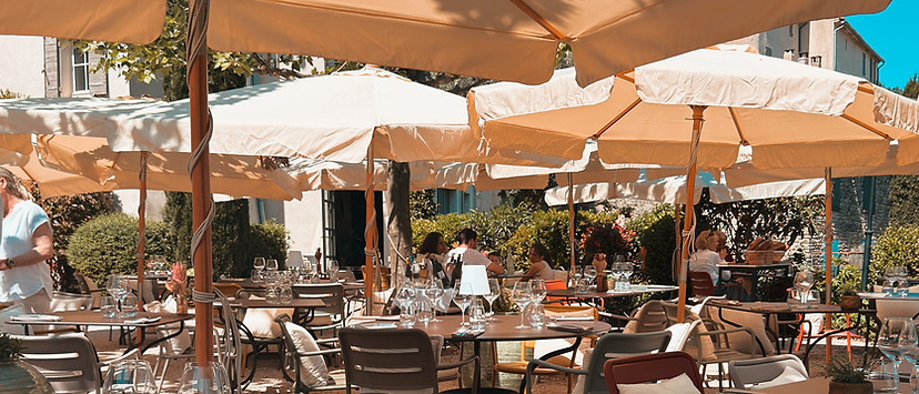 Terrasse de Monsieur Tu, parasols crème en enfilade, tables dressées avec chaises dépareillées