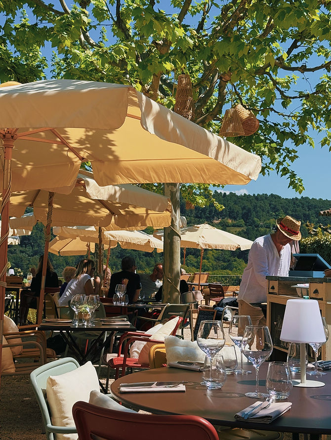 Terrasse de Monsieur Tu sous un platane, parasols crème, vue sur les collines du Luberon au loin